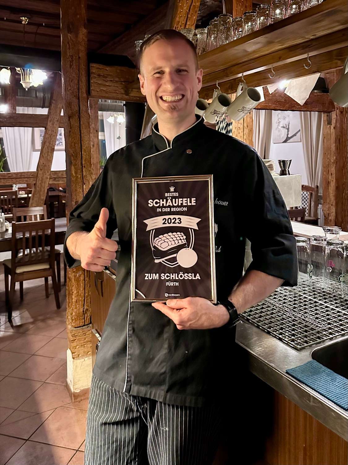 Christian Umhauer in a black chef’s jacket holding the nordbayern.de certificate “Bestes Schäufele in der Region 2023”