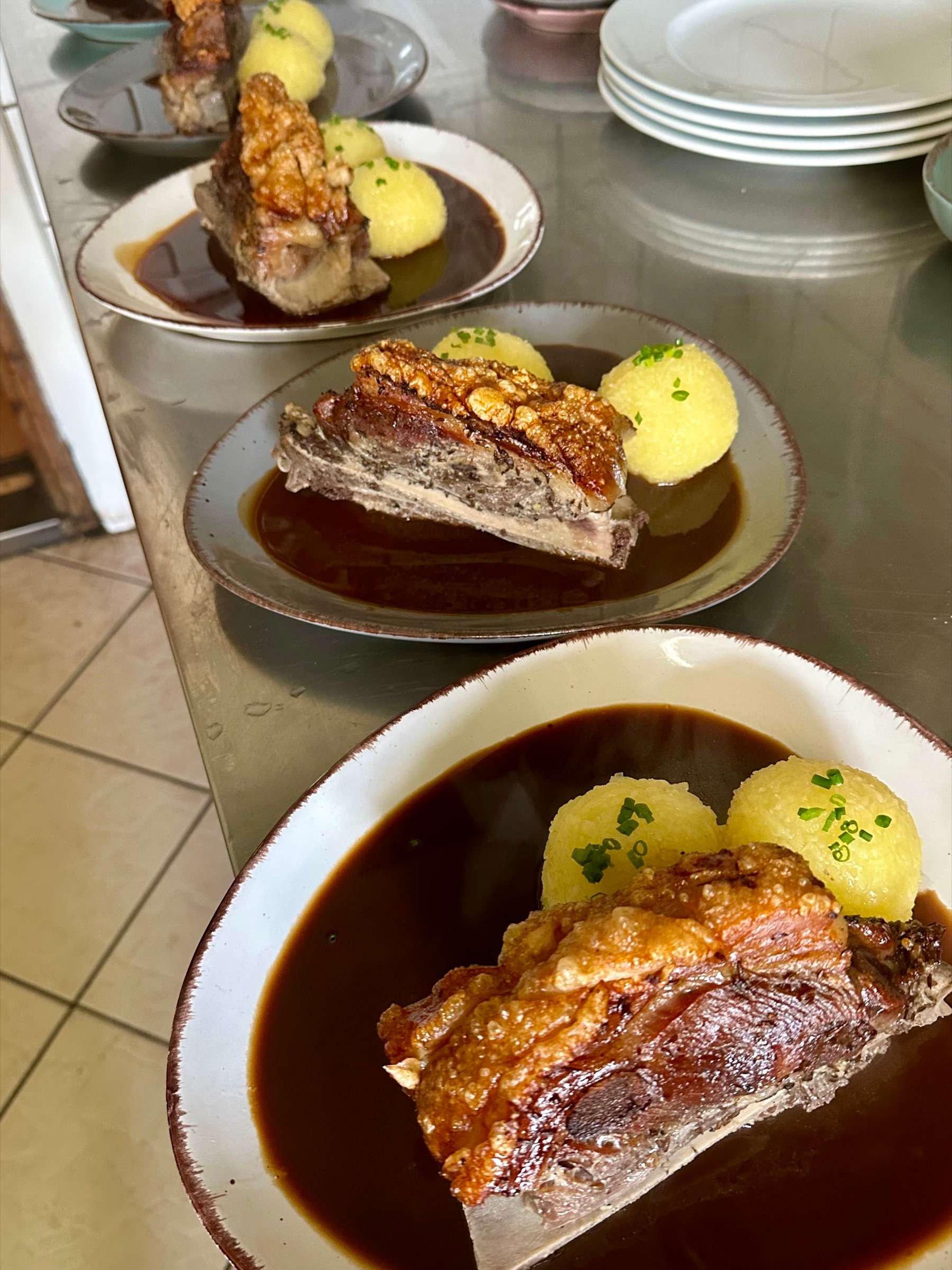 Plates of Schäufele with potato dumplings and dark gravy on the pass in our kitchen